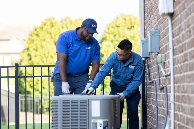 Two HVAC technicians inspecting a residential outdoor air conditioner