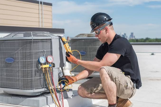 Rooftop technician checking an air conditioner with gauges and a meter